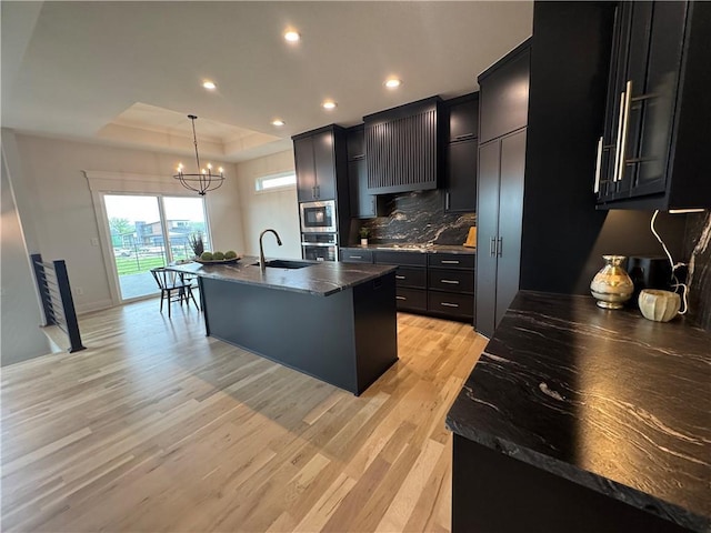 kitchen with dark cabinets, light wood-style flooring, a chandelier, stainless steel appliances, and dark countertops