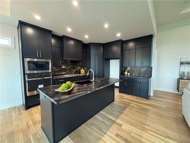 kitchen featuring dark stone countertops, a sink, appliances with stainless steel finishes, light wood finished floors, and backsplash