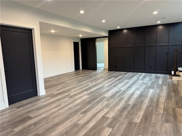 unfurnished living room with light wood finished floors, recessed lighting, a decorative wall, and baseboards
