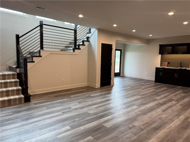 unfurnished living room featuring visible vents, recessed lighting, wood finished floors, baseboards, and stairway