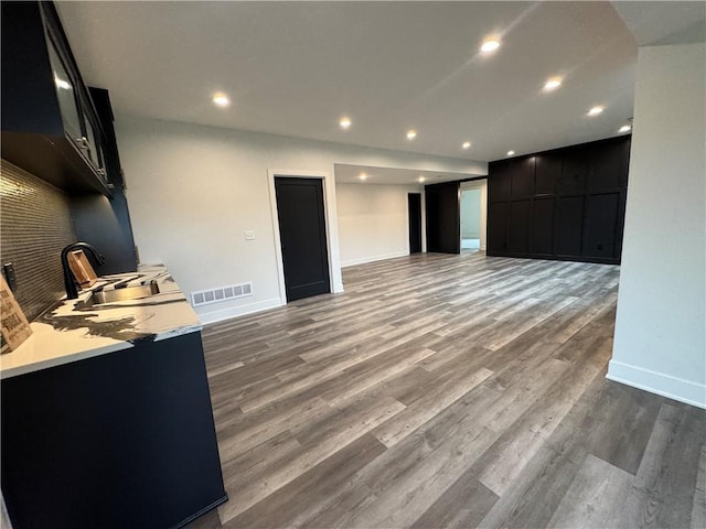 unfurnished living room with recessed lighting, a sink, visible vents, baseboards, and wood finished floors