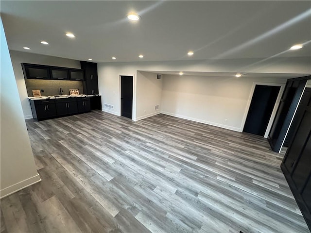 unfurnished living room with wet bar, baseboards, wood finished floors, and visible vents