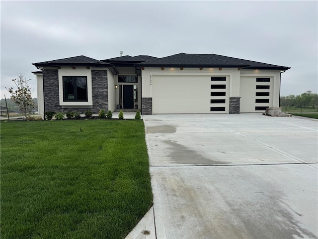 prairie-style home featuring a front lawn, driveway, stone siding, and an attached garage