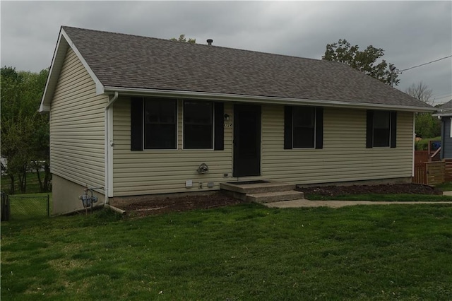 view of front of house with a front yard, roof with shingles, and fence