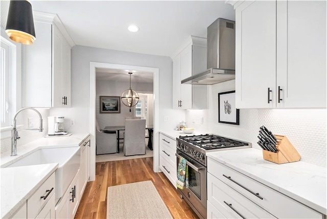 kitchen featuring wall chimney range hood, light wood-type flooring, high end range, a sink, and white cabinetry