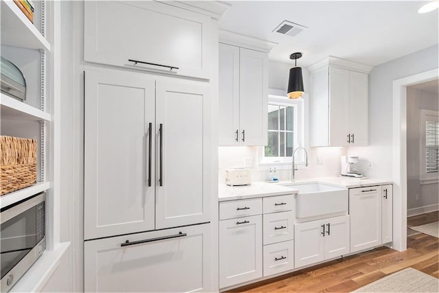 kitchen with a sink, light wood finished floors, white cabinetry, stainless steel microwave, and visible vents