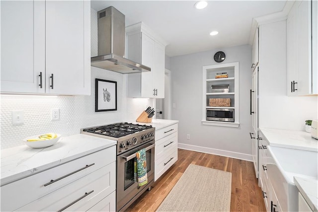 kitchen featuring wood finished floors, wall chimney exhaust hood, white cabinets, tasteful backsplash, and appliances with stainless steel finishes