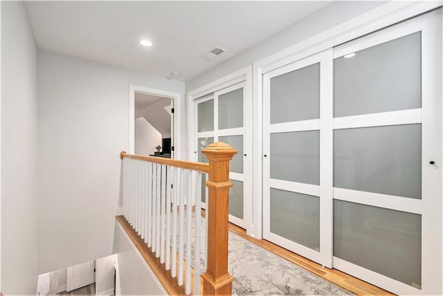 hall with recessed lighting, visible vents, wood finished floors, and an upstairs landing