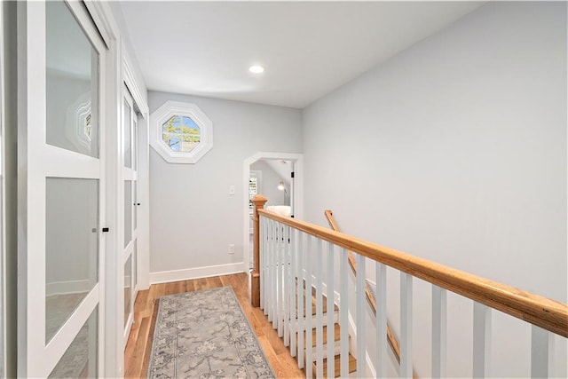 corridor featuring light wood-style floors, arched walkways, recessed lighting, baseboards, and an upstairs landing