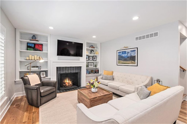 living area featuring baseboards, visible vents, a fireplace with flush hearth, and wood finished floors
