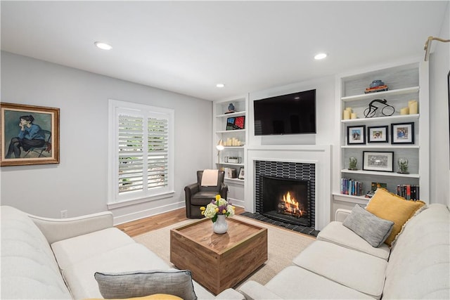 living area featuring wood finished floors, baseboards, recessed lighting, built in shelves, and a tile fireplace