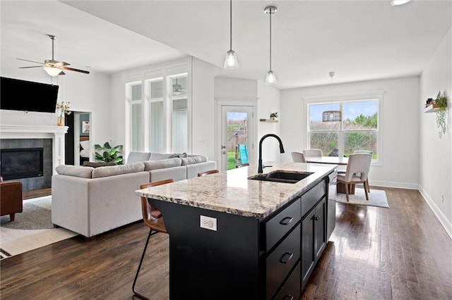 kitchen featuring a ceiling fan, dark wood-style flooring, a tile fireplace, a sink, and dark cabinetry