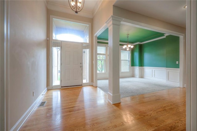 entrance foyer with decorative columns, visible vents, crown molding, wood finished floors, and a notable chandelier