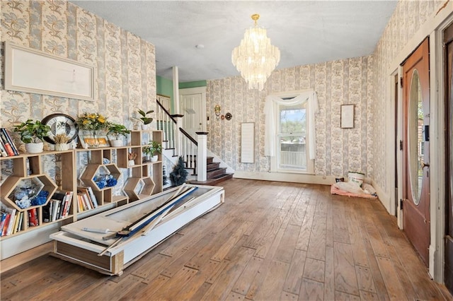 misc room featuring wood-type flooring, wallpapered walls, stairs, and a notable chandelier