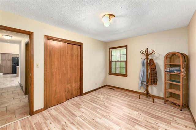 2501 Olde Creek Ct S, Leavenworth, KS 66048 - unfurnished bedroom featuring light wood finished floors, a closet, black fridge with ice dispenser, and a textured ceiling