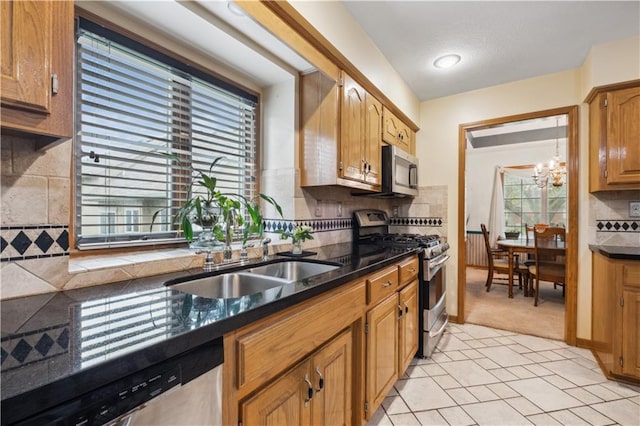 kitchen with brown cabinetry, backsplash, appliances with stainless steel finishes, a sink, and a notable chandelier