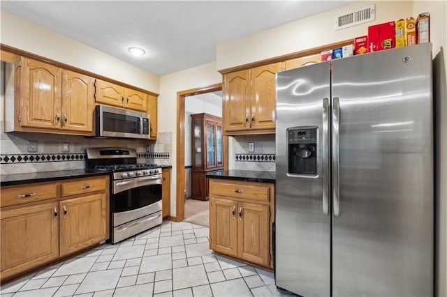 kitchen with dark countertops, appliances with stainless steel finishes, brown cabinetry, backsplash, and visible vents