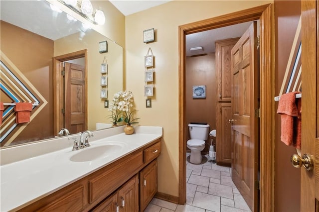 bathroom with stone tile floors, toilet, baseboards, and vanity