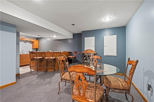 dining room with bar area, baseboards, a textured ceiling, and light colored carpet