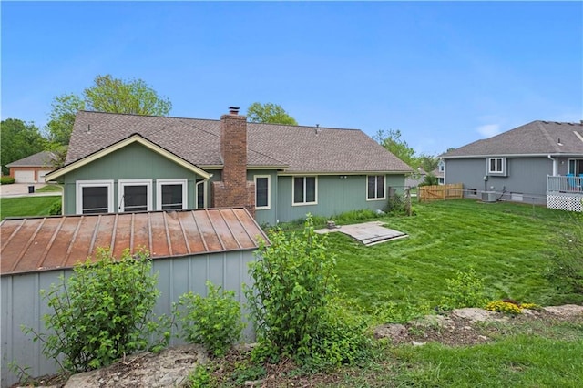 back of house with a lawn, fence, a chimney, and a shingled roof