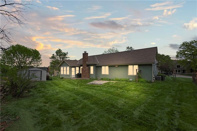 back of property with fence, central air condition unit, a storage shed, a chimney, and a lawn
