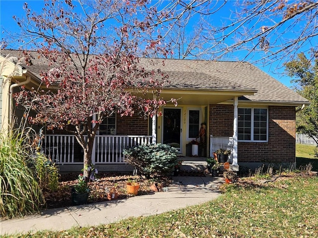 view of front of house featuring roof with shingles, covered porch, a front yard, and brick siding