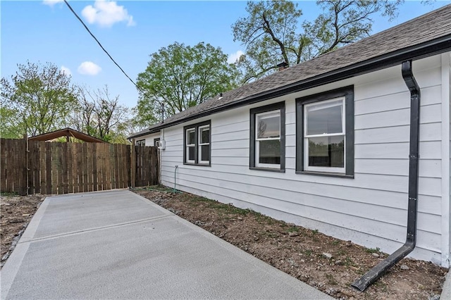 view of home's exterior featuring fence, a shingled roof, and a patio