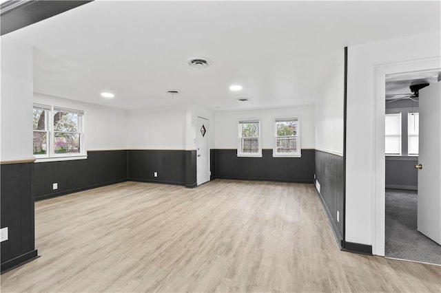 spare room featuring wood finished floors, visible vents, a wainscoted wall, and ceiling fan