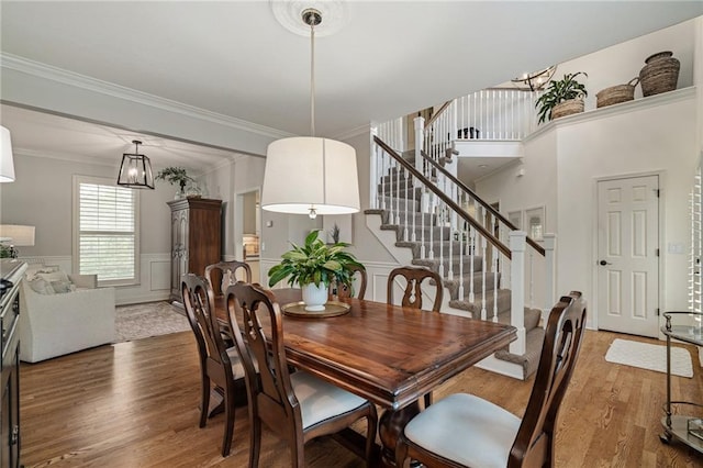 dining area with wainscoting, a decorative wall, stairs, wood finished floors, and ornamental molding