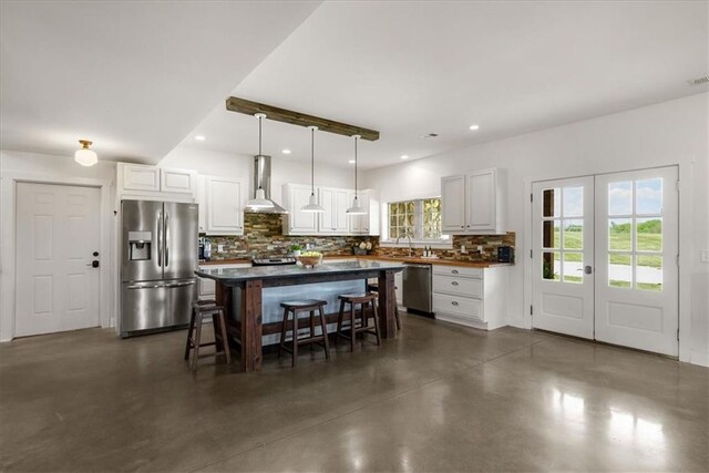 kitchen featuring stainless steel appliances, wall chimney exhaust hood, concrete flooring, a kitchen breakfast bar, and backsplash