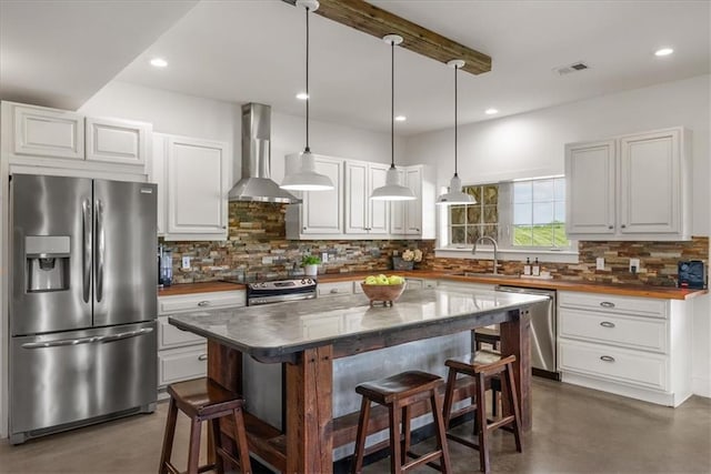 kitchen featuring appliances with stainless steel finishes, wall chimney exhaust hood, finished concrete floors, a breakfast bar area, and recessed lighting