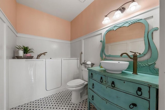 bathroom featuring wainscoting, vanity, toilet, and a decorative wall