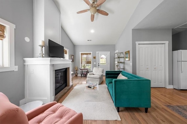 living room featuring vaulted ceiling, ceiling fan, a glass covered fireplace, and wood finished floors