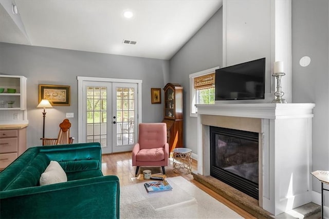 living room with french doors, wood finished floors, vaulted ceiling, and a glass covered fireplace