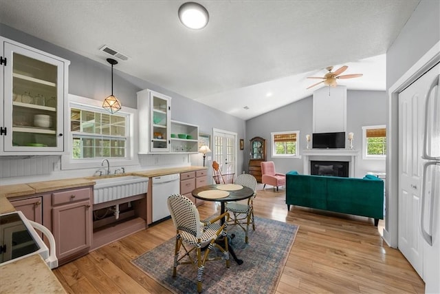dining room featuring vaulted ceiling, a ceiling fan, light wood finished floors, and a glass covered fireplace