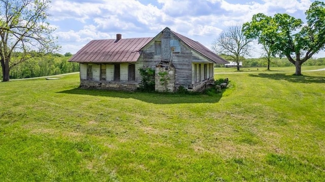 view of side of property with a yard, stone siding, a chimney, metal roof, and a standing seam roof
