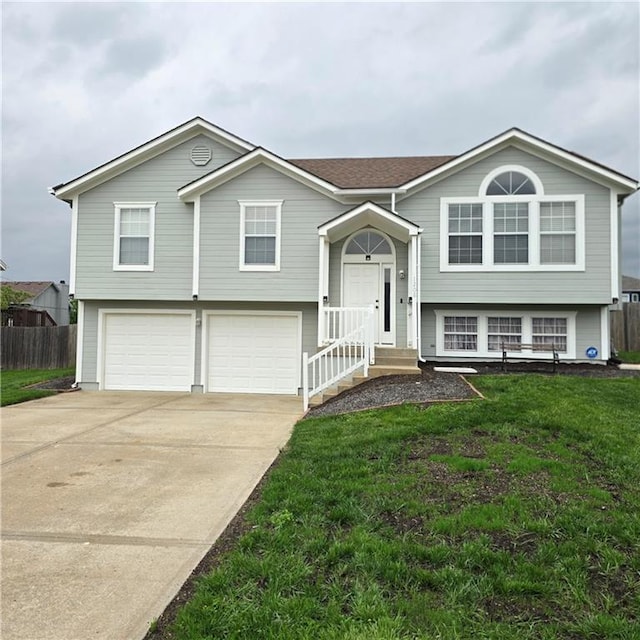raised ranch with a front lawn, driveway, an attached garage, and fence