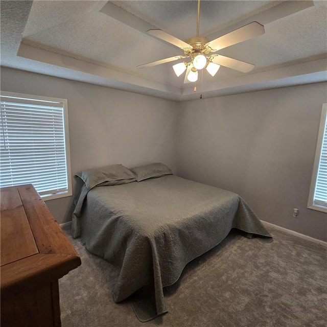 carpeted bedroom with baseboards, ceiling fan, multiple windows, and a tray ceiling
