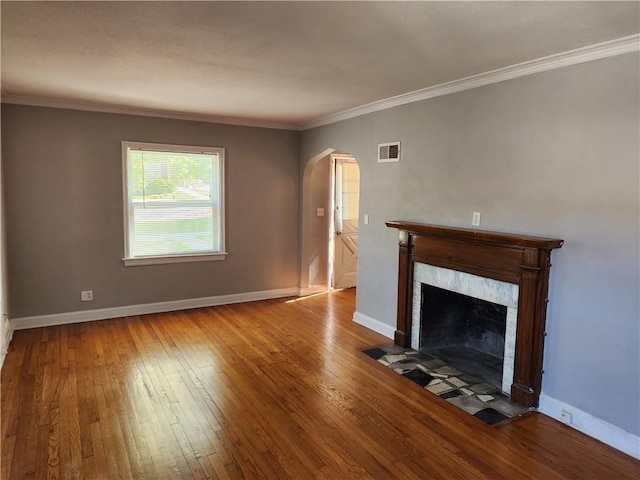 unfurnished living room featuring arched walkways, hardwood / wood-style floors, a fireplace, baseboards, and ornamental molding