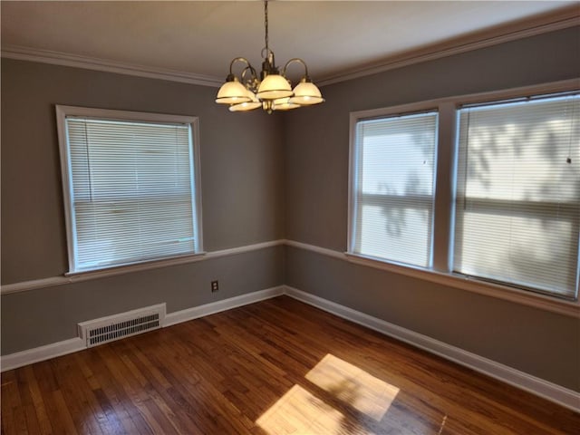 empty room with a chandelier, wood finished floors, baseboards, and crown molding