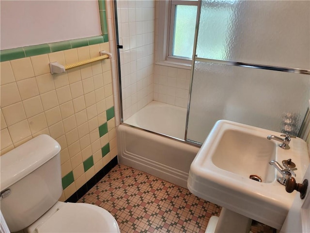 full bath with tile walls, toilet, a sink, and combined bath / shower with glass door