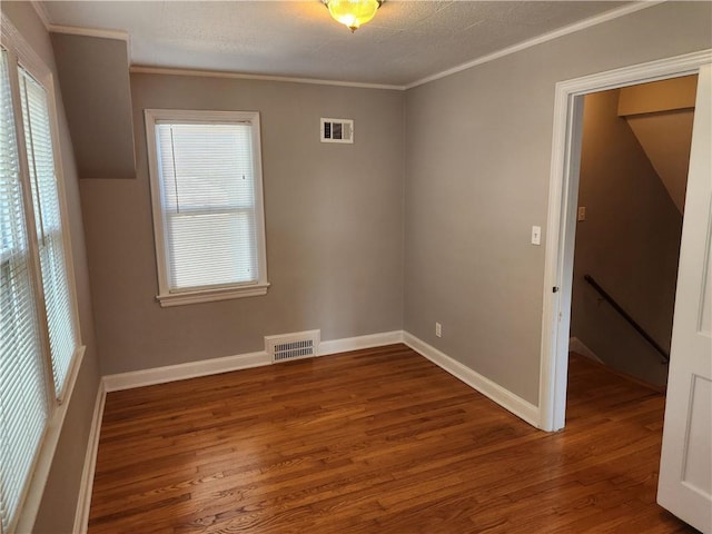 empty room featuring wood finished floors, crown molding, and baseboards