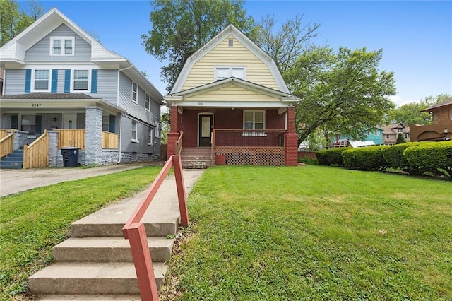 3245 Victor St, Kansas City, MO 64128 - view of front facade with covered porch, a gambrel roof, brick siding, and a front lawn