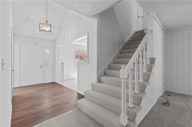 foyer with a chandelier, wood finished floors, stairs, a textured ceiling, and lofted ceiling