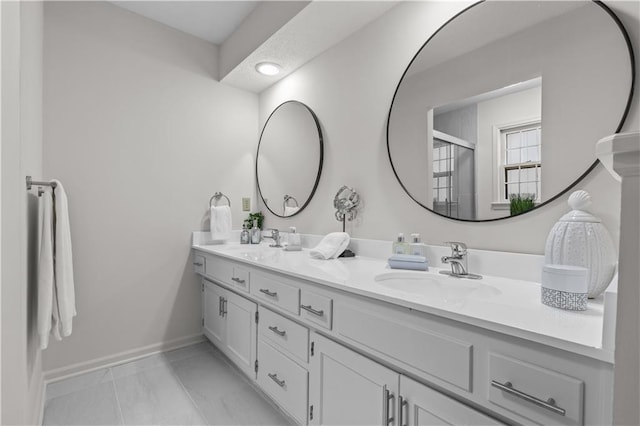 full bathroom featuring baseboards, a shower with shower door, double vanity, and a sink