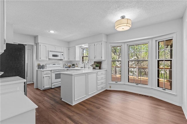 kitchen featuring visible vents, white appliances, a textured ceiling, and a peninsula