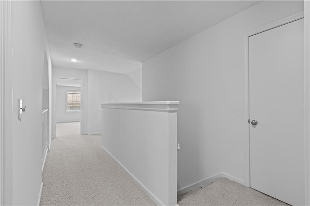 corridor featuring an upstairs landing, baseboards, and light carpet