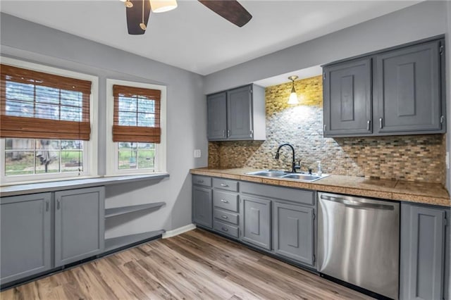 kitchen featuring a ceiling fan, stainless steel dishwasher, gray cabinetry, a sink, and tile counters