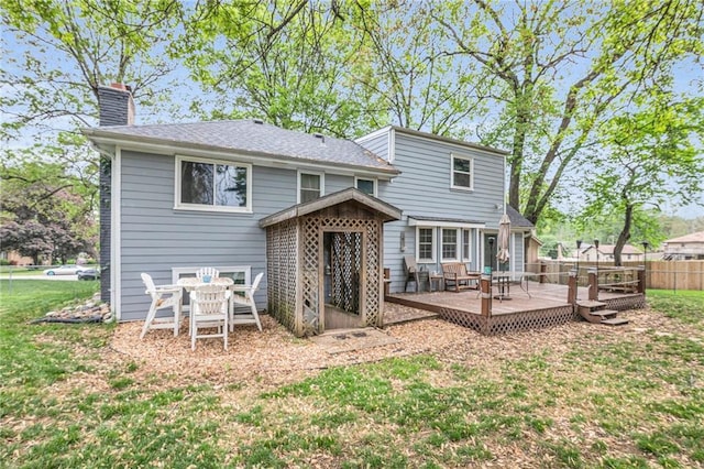 back of property featuring fence, a yard, a chimney, and a deck