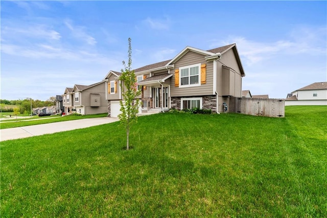 split foyer home with stone siding, a garage, fence, concrete driveway, and a front lawn